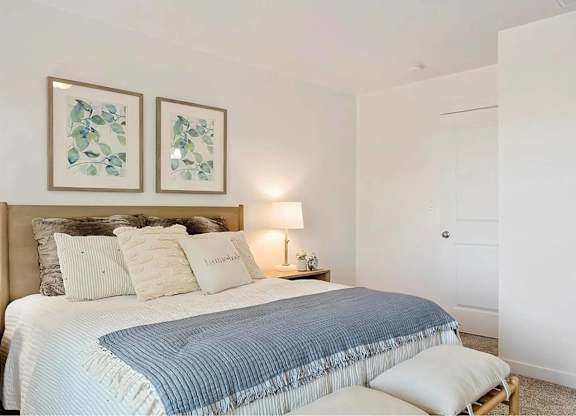 A bedroom with a bed, pillows, a lamp, and two pictures on the wall.