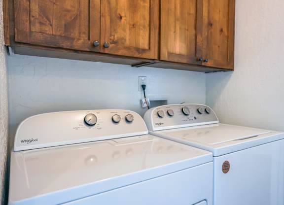 A white washing machine and dryer are sitting under a wooden cabinet.