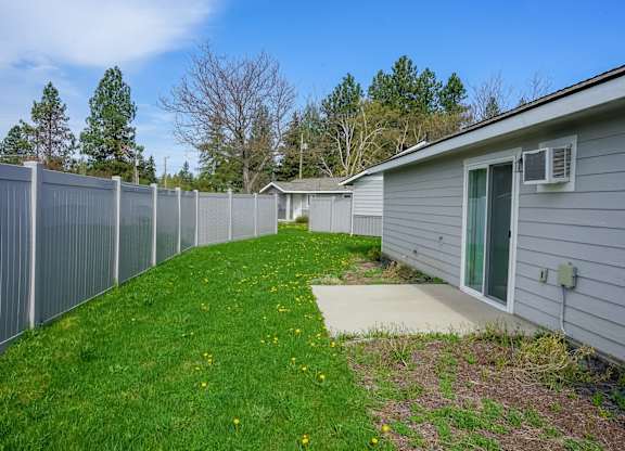 A grey fence separates a green lawn from a grey house.