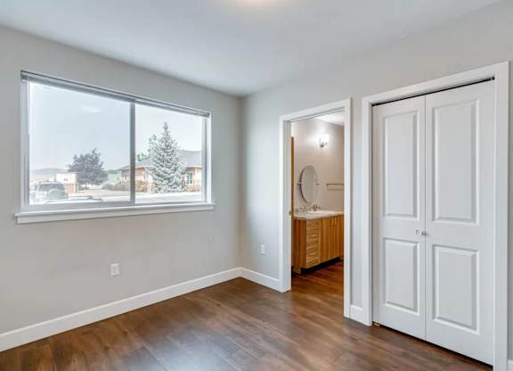 A room with a window, wooden floor, and a white door.