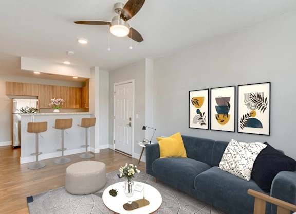 A living room with a grey couch, a round ottoman, a coffee table with a vase of flowers, and three framed pictures on the wall.