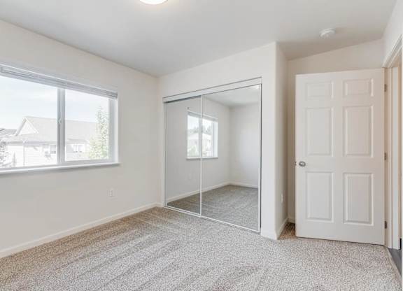 A room with a carpeted floor, a white door, and a large window with a view of a house across the street.