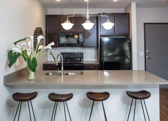 A kitchen with a white countertop and brown bar stools.