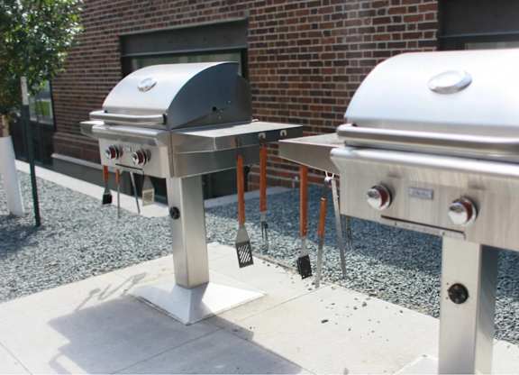 Two silver barbecue grills are placed on a gravel surface.