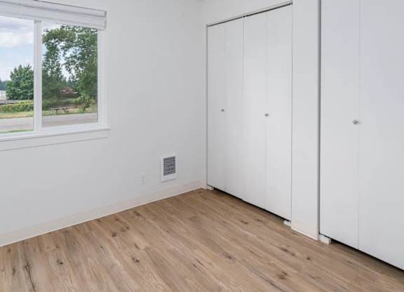 A room with white walls, a window, and a wooden floor.