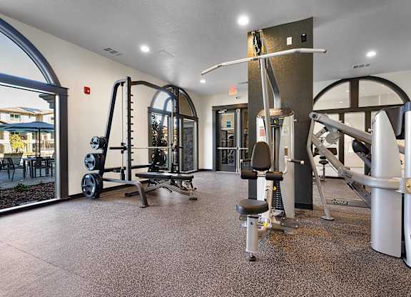 A gym with a variety of equipment including a leg press machine, a chest press machine, a lat pulldown machine, a cable machine, and a squat rack.