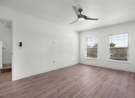 an empty living room with a ceiling fan and two windows