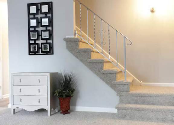 A staircase with a metal railing and a potted plant next to a white chest of drawers.