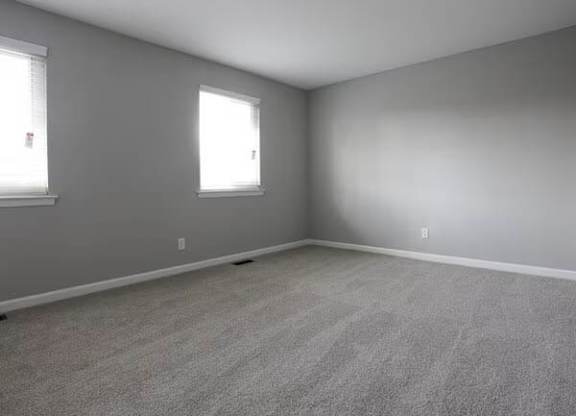 A room with grey walls and carpeted floor with two windows.