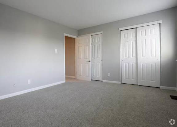 A room with grey carpet and white walls with two doors.