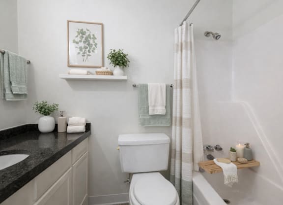 A white toilet sits in a bathroom next to a sink and a bathtub.