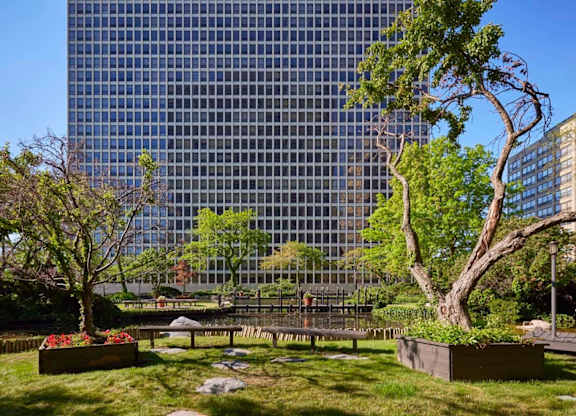 A park with a bench and a tree in front of a glass building.