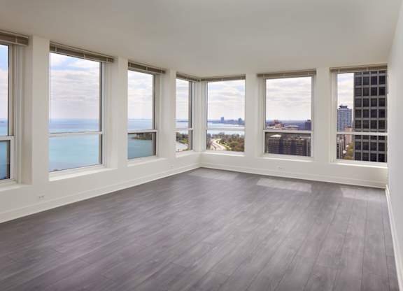 A large empty room with wooden floors and windows overlooking a body of water.