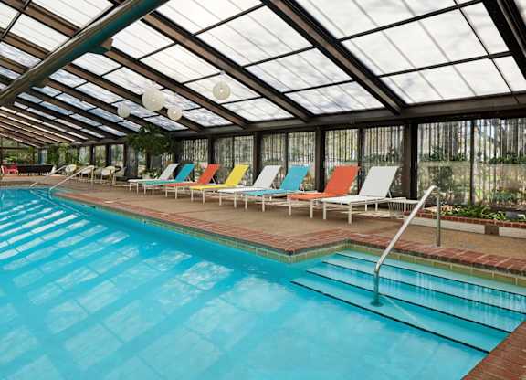 A large indoor swimming pool with a glass ceiling and colorful lounge chairs.