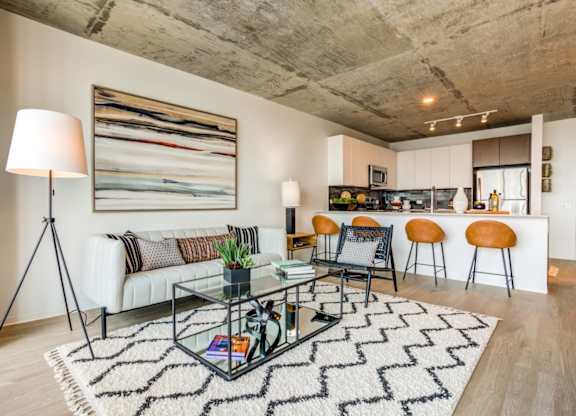 A modern living room with a glass coffee table and a large abstract painting on the wall.