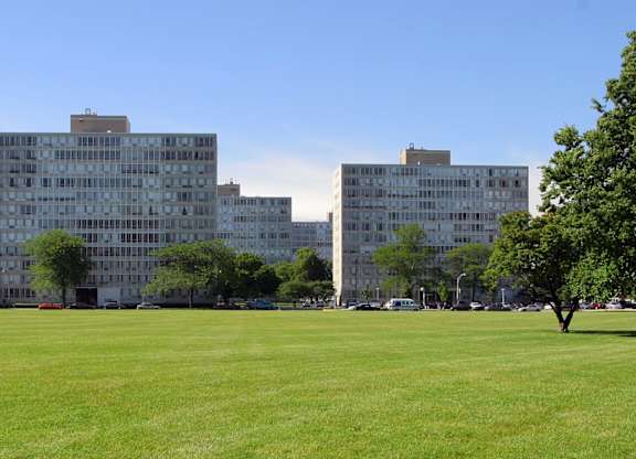 A grassy field with trees and buildings in the background.