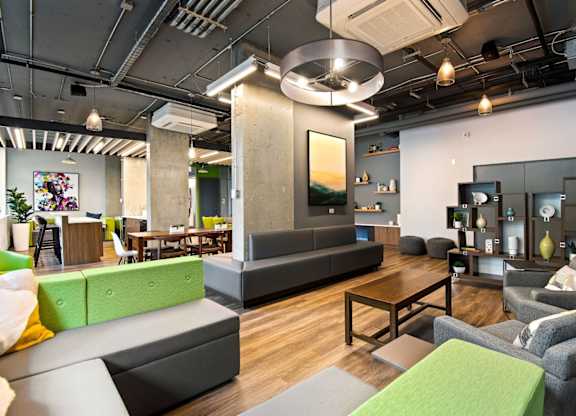 A modern living room with a grey couch, a green ottoman, and a wooden coffee table.