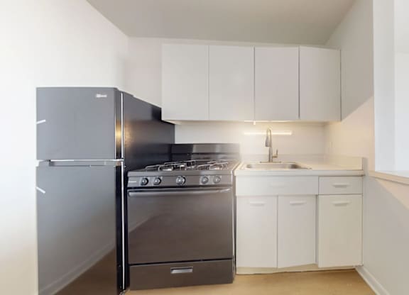 A kitchen with a black fridge, stove and white cabinets.