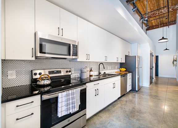 A modern kitchen with white cabinets and black countertops. at Judson Mill Lofts and The Jenny & Westervelt in Greenville, SC