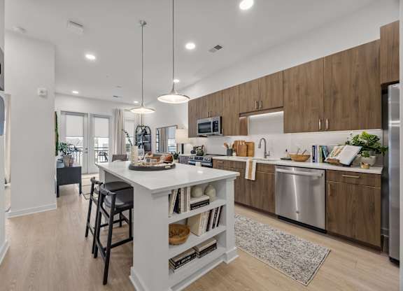 A modern kitchen with a white island and wooden cabinets.at Adler Montford Park + Drexel Townes, Charlotte, NC, 28209