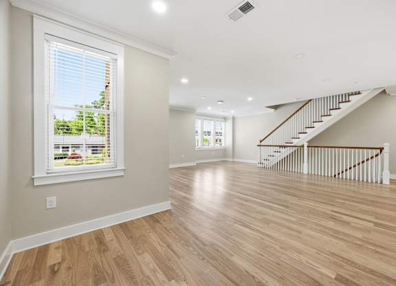 A spacious room with wooden floors and a staircase.