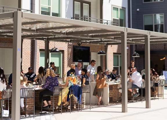 People are sitting at tables under a canopy outside a building.