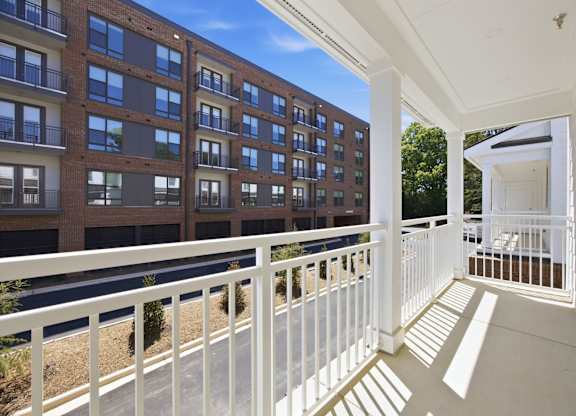 A balcony with white railings overlooks a parking lot and a building.