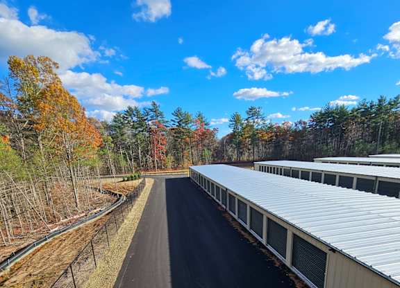 Drive-up self storage units with green roll-up doors and paved access lanes at Rochester Self Storage in Rochester, MA.