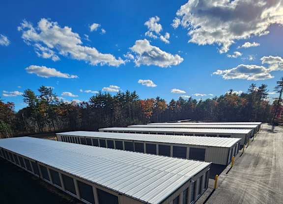 Long row of drive-up self storage units with metal roll-up doors and fresh asphalt at Rochester Self Storage in Rochester, MA.