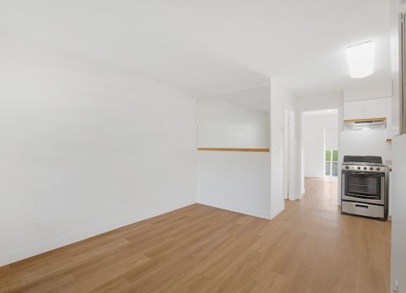 A spacious room with wooden flooring and a stove in the corner.