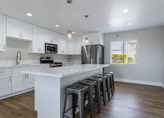 A kitchen with white cabinets and a large island with stools.