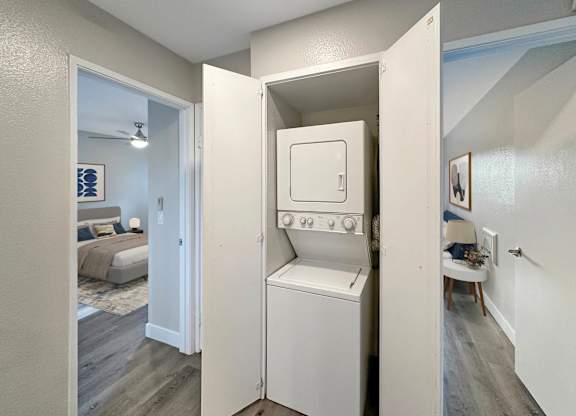 A small white washing machine is in a cabinet in a bedroom.