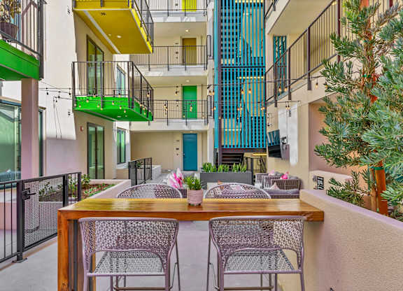 A patio with a table and chairs overlooks a courtyard with a fence and a tree.
