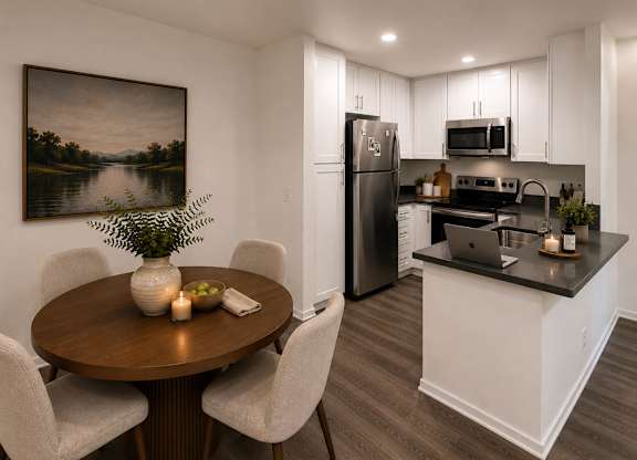 A dining room with a wooden table and chairs, a fridge, a microwave, and a painting on the wall.
