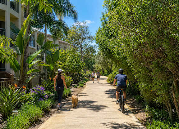 A woman walking a dog on a path with a man riding a bike behind her.