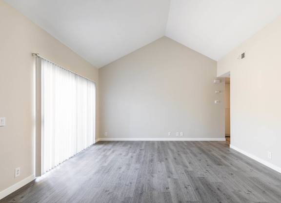 A room with a wooden floor and a window with white curtains.