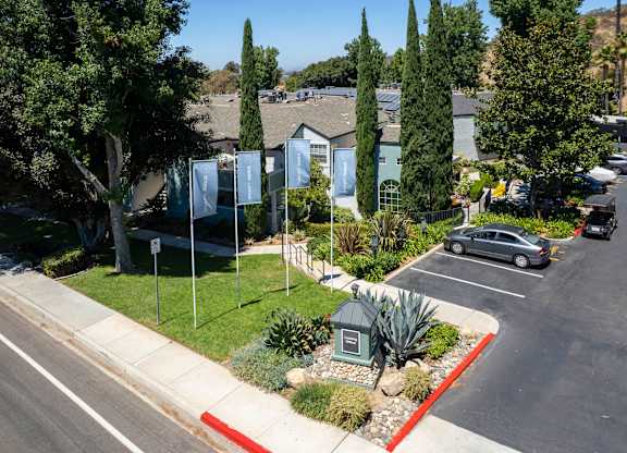 A street view of a residential area with a house, trees, and a parking lot.