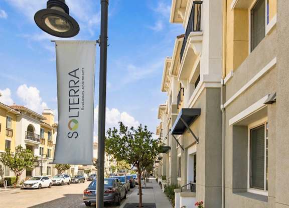 A street view of a Solterra apartment complex with a sign, lamp post and parked cars.