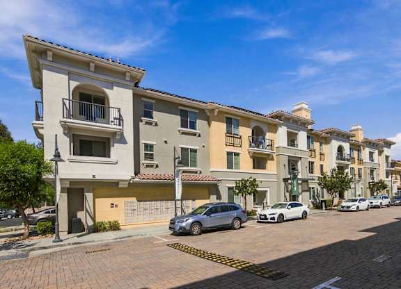 A row of apartment buildings with cars parked in front.