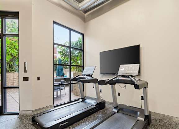 A treadmill and a stationary bike are in a room with a TV and a laptop on a stand.