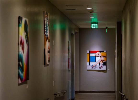 A hallway with a green exit sign and artwork on the walls.