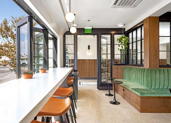 A long white table with orange chairs is in front of a window.