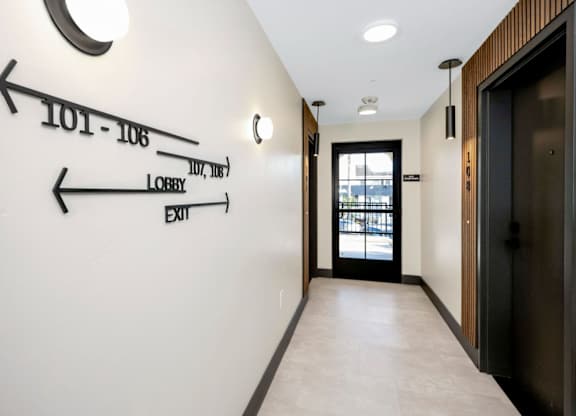 A hallway with a white wall and a black door.