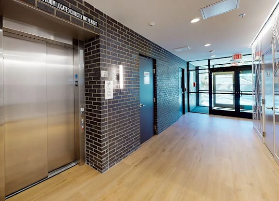A hallway with a brick wall and a wooden floor leading to a glass door.