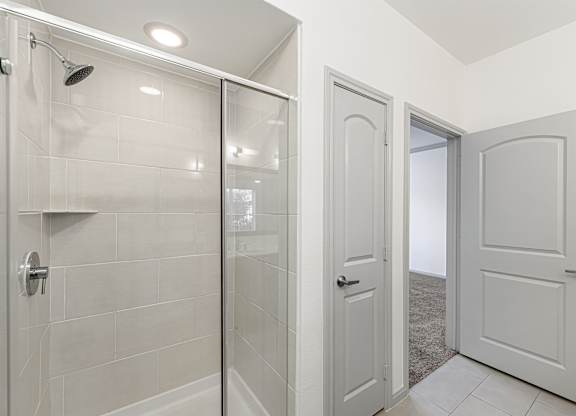 A white bathroom with a glass shower door and a white tiled shower wall.