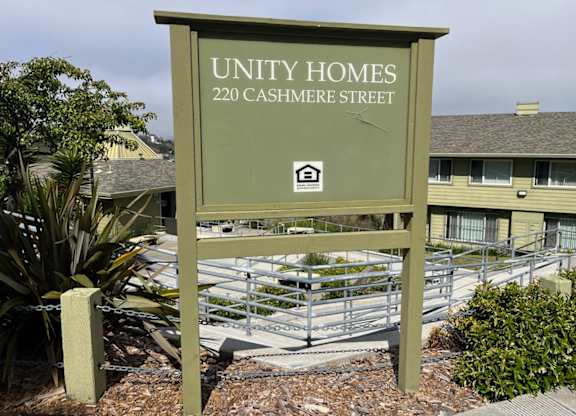 A sign for Unity Homes at 220 Cashmere Street stands in front of a building.