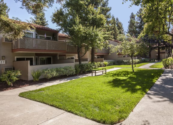a sidewalk in front of an apartment building with grass and trees at Valley Plaza Villages, Pleasanton, California