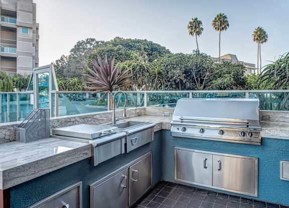 A modern outdoor kitchen with stainless steel appliances and a view of a hill with palm trees. at Esprit Apartments, Marina del Rey, CA, 90292