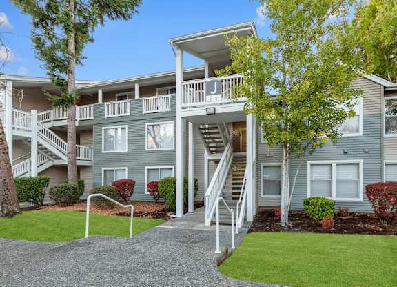 Gray apartment building with exterior stairs, balconies, and landscaped grounds.