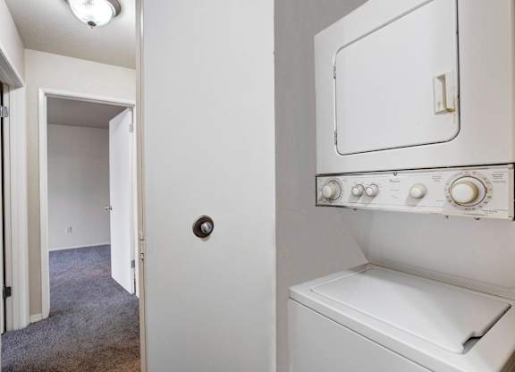 Laundry closet with a stacked washer and dryer beside the hallway.
